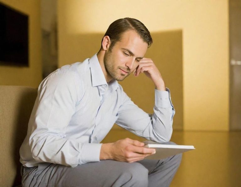 Junger Mann in Hemd sitzt nachdenklich mit einem Tablet in der Hand.